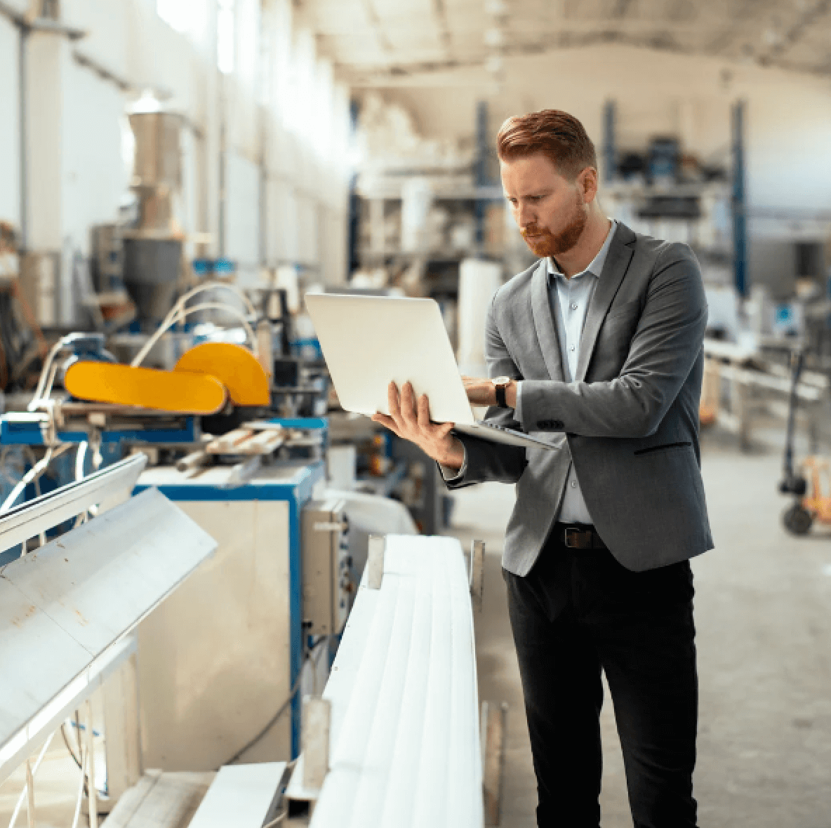 man in a suit typing on a laptop in a factory